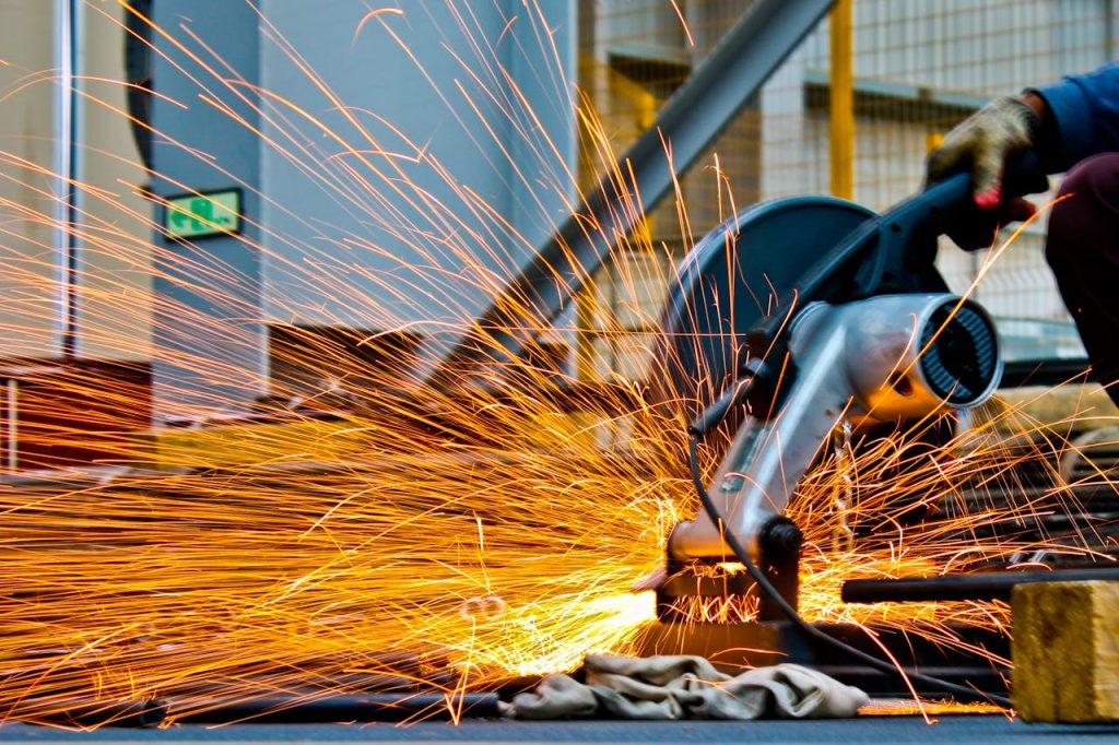 a man grinds metal with a power tool, sparks illuminating the workspace