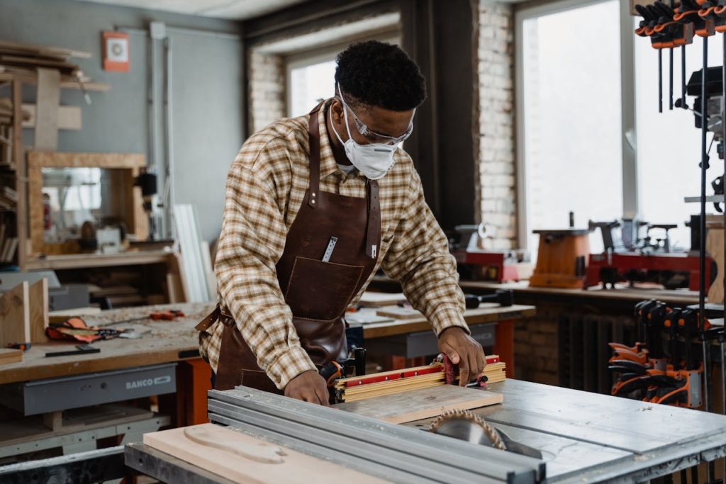 a man wearing a mask is diligently using a table saw