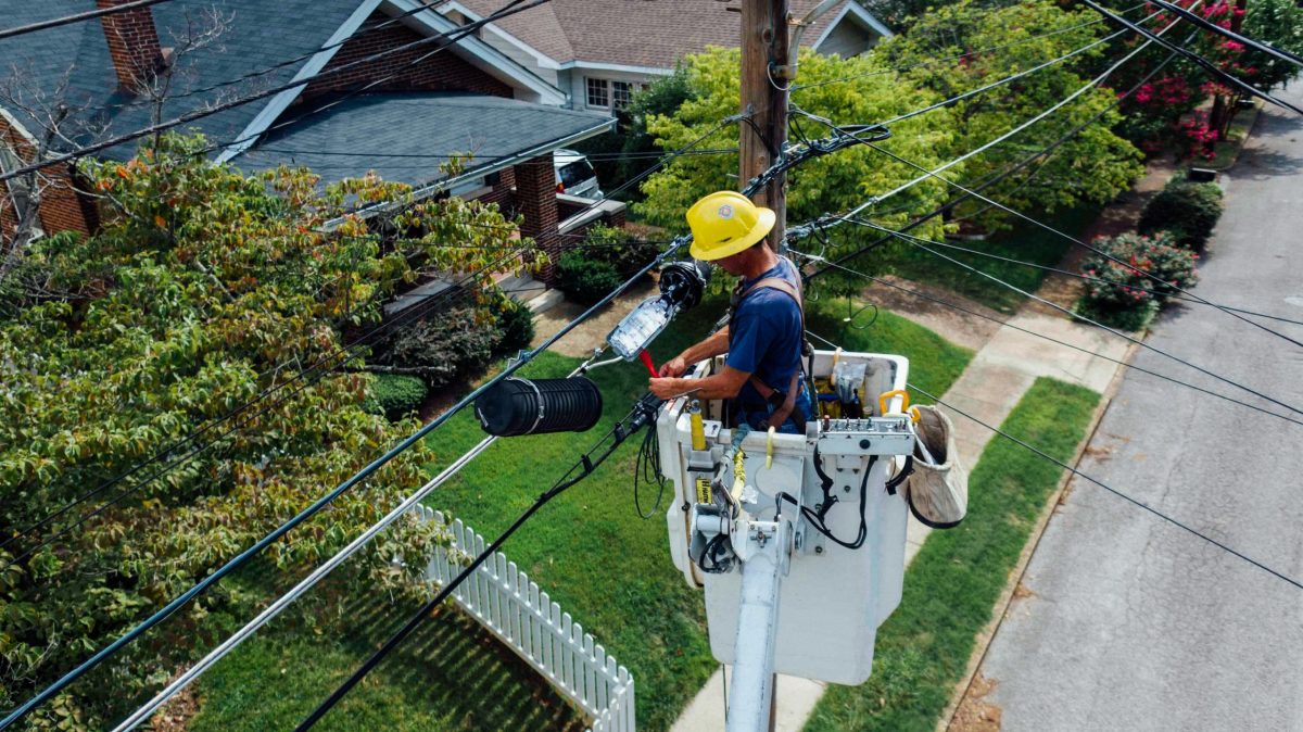 an electrician works on a power pole near a house