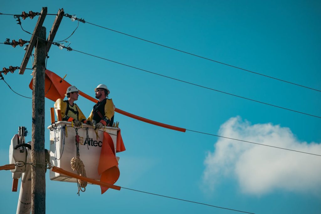 electricians standing on a power pole attaching orange flags to ensure safety
