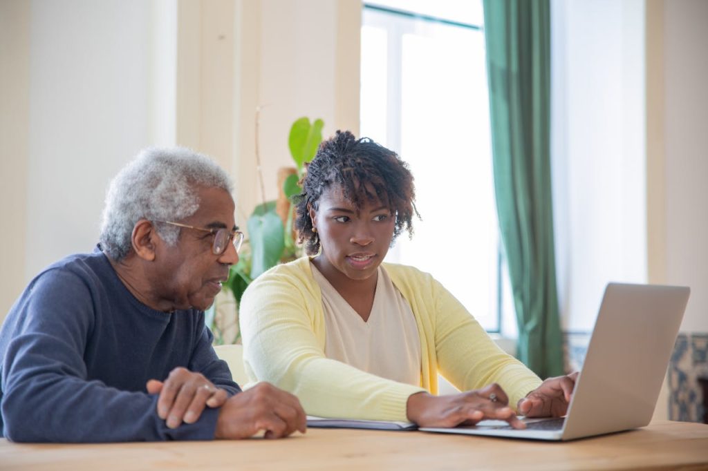 an older man and woman at a table with a laptop