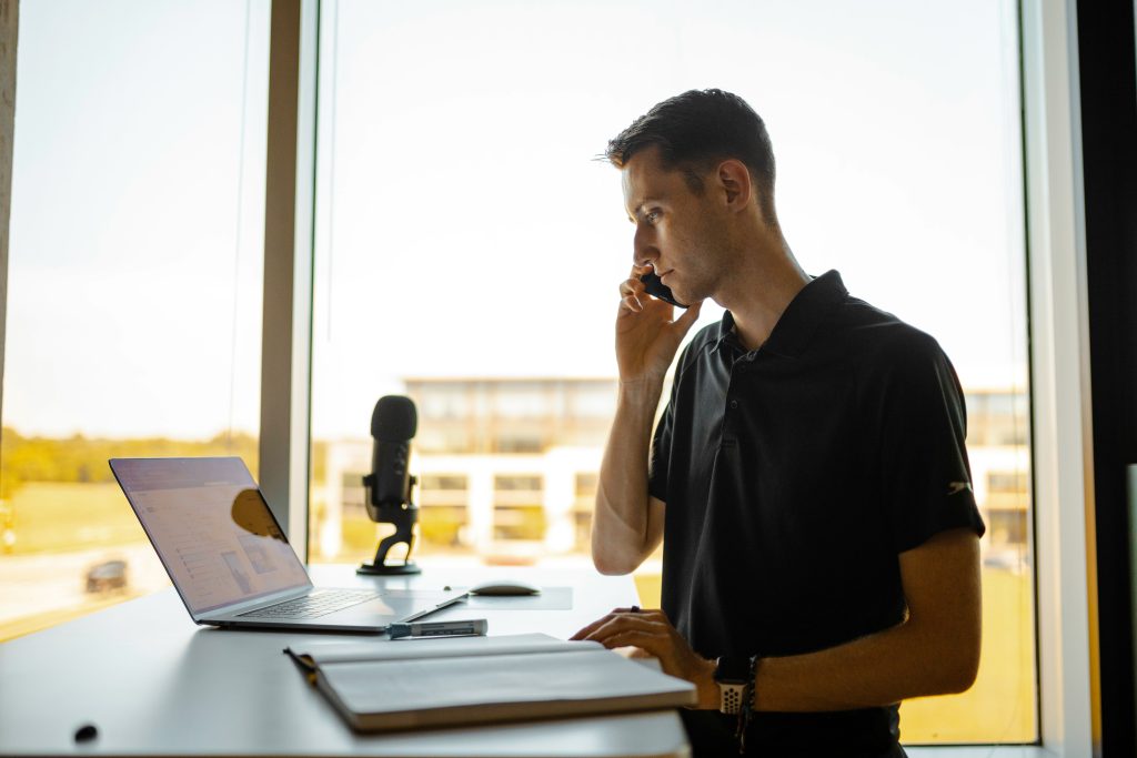 a man working at a desk with a laptop and phone