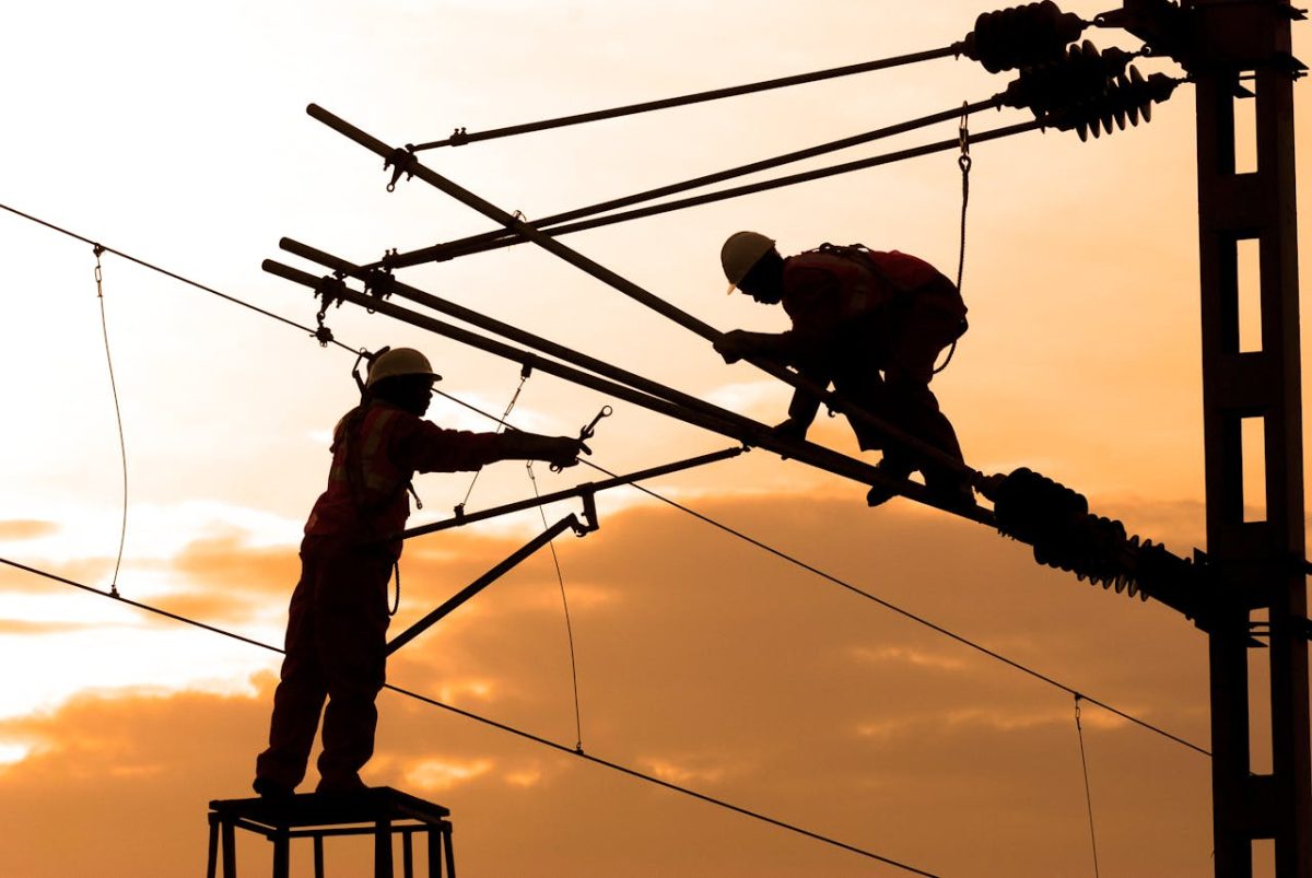 at sunset, two men are engaged in work on a power pole