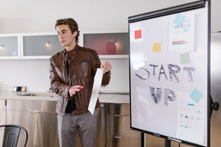 man is positioned in front of a whiteboard marked with start up