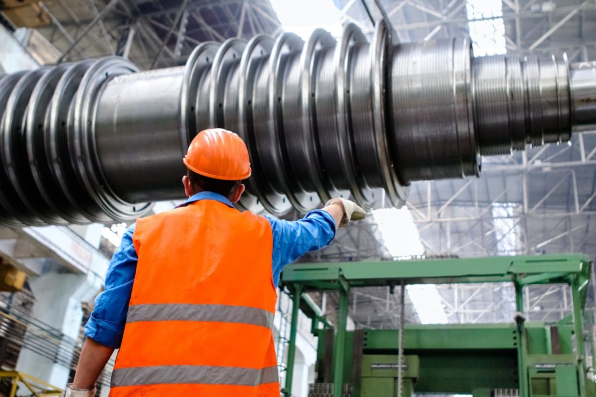 a man wearing an orange vest is positioned next to a large metal pipe