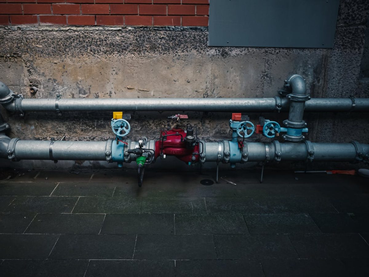 red fire hydrant connected to pipes, set against brick wall