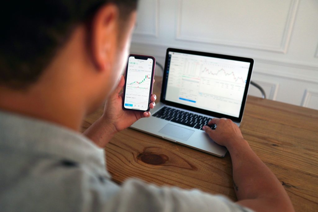 a man engaged in checking stock market information using both a smartphone and a laptop