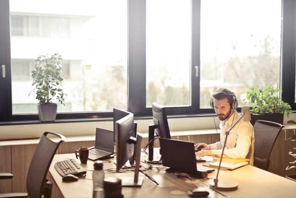A man in a white shirt and headphones focused on his computer, providing customer support.