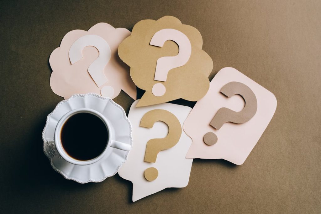 A coffee cup with question marks and paper speech bubbles on a brown background.