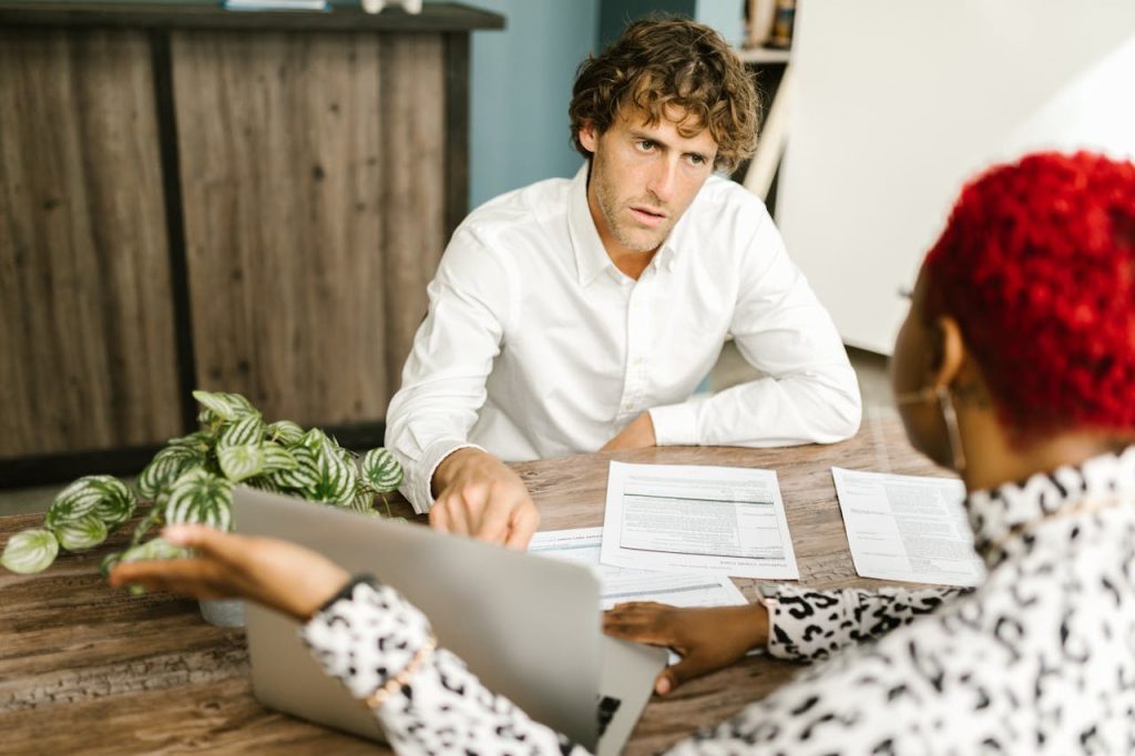 an insurance broker, sit at a table with a laptop, discussing options with a client
