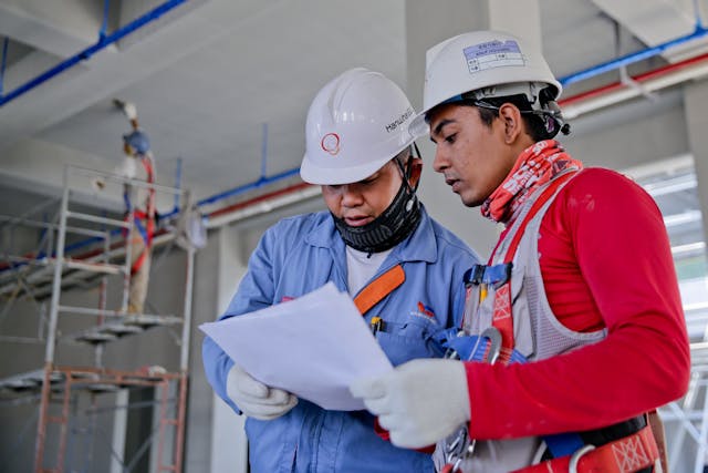 two men in safety vests and hard hats focused on a paper