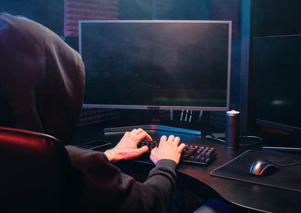 a person in a hoodie sits at a computer, focused on the screen